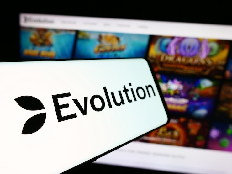 에볼루션(Evolution) 로고가 스마트폰 화면에 표시되어 있고, 배경에는 다양한 온라인 카지노 게임 화면이 흐릿하게 보인다.
